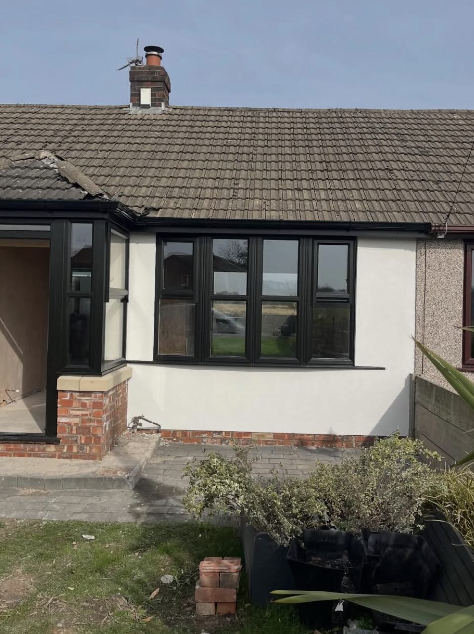 Bungalow front rendered smooth white, next to a neighbouring wall still in pebbledash