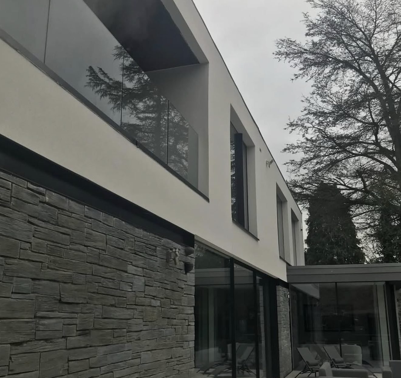 Contemporary house with a white rendered upper storey over dark stone cladding and a glass balcony