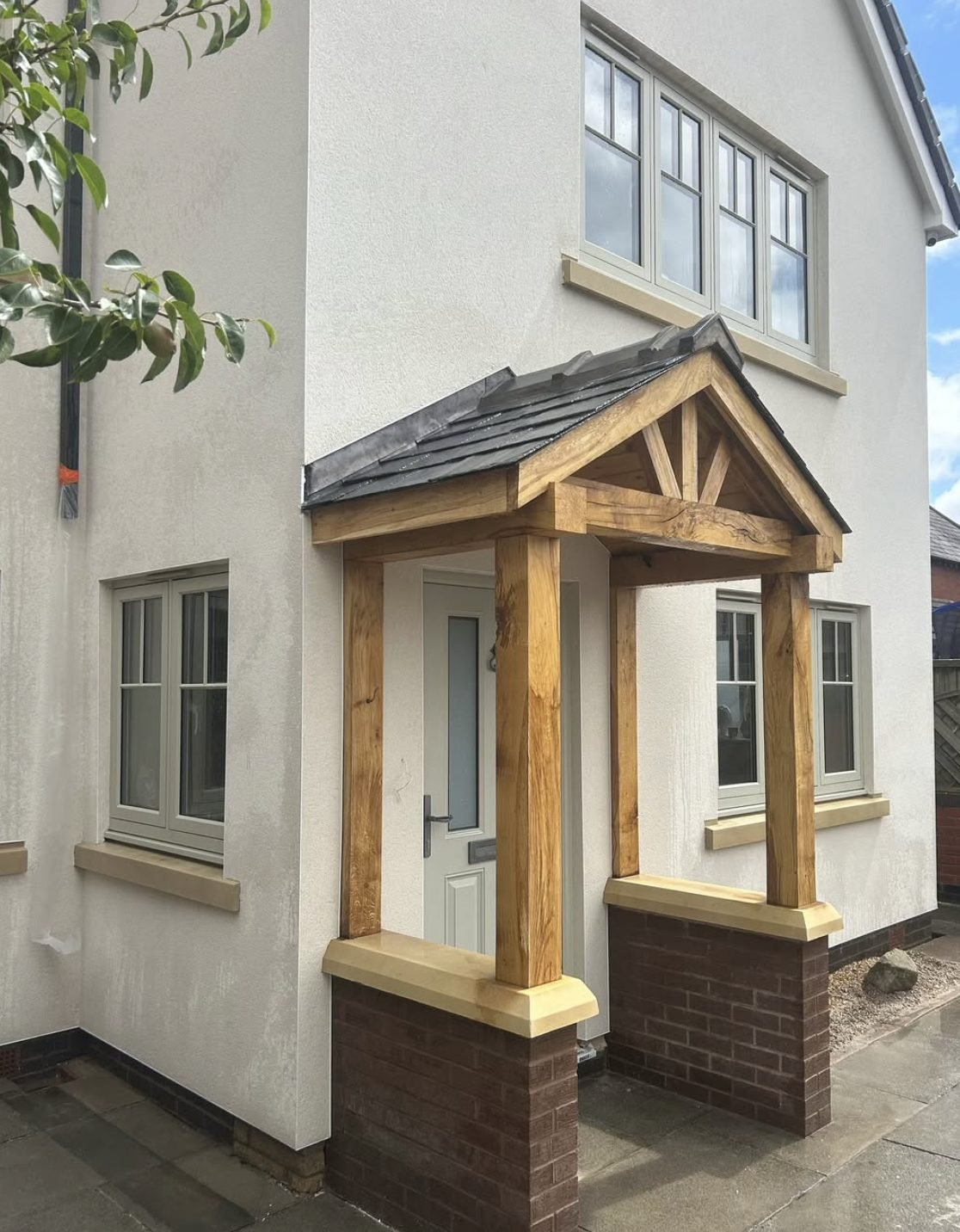 Cream rendered house with a green oak porch on brick piers