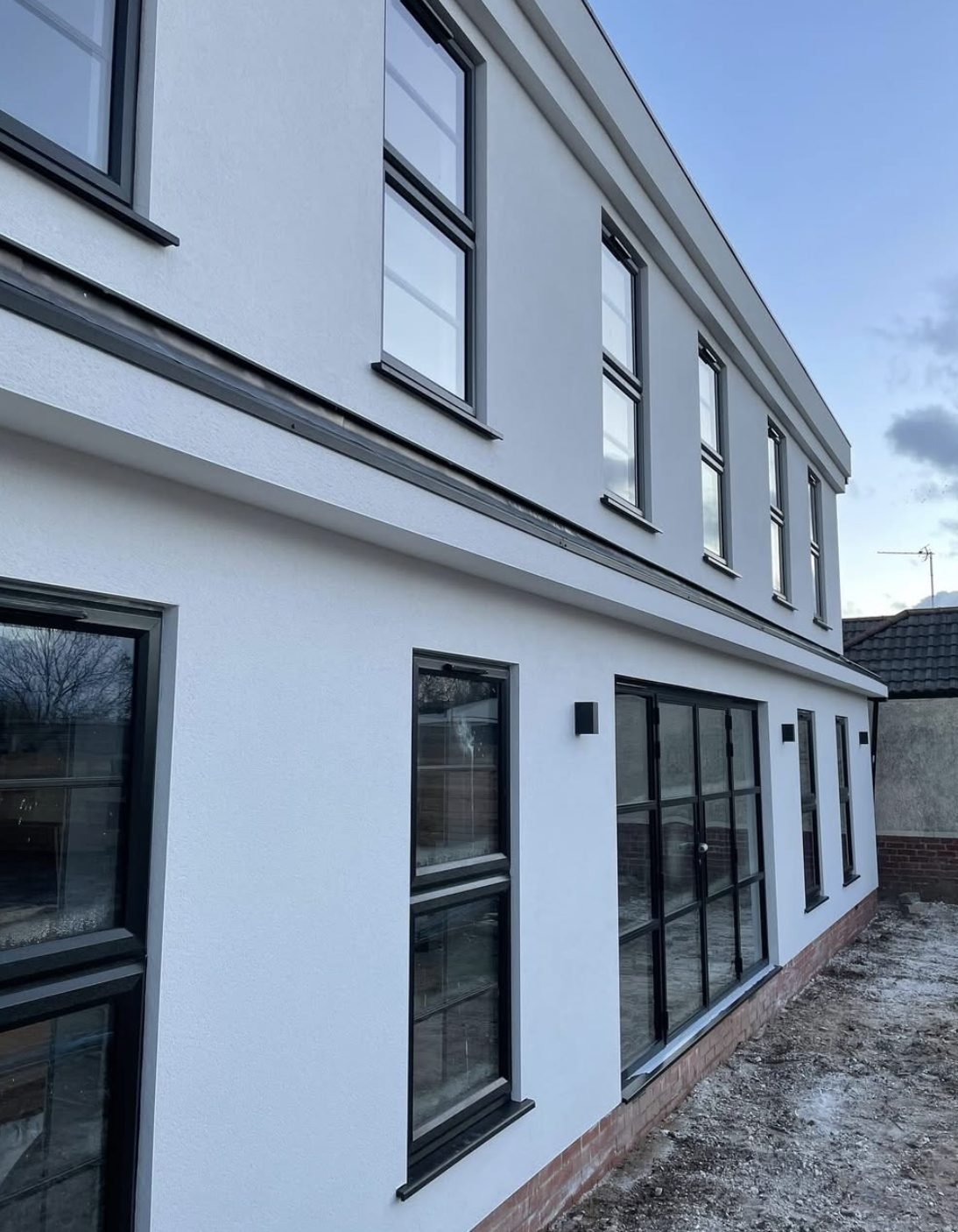 Two-storey side elevation in smooth white render with a dark band course and black windows